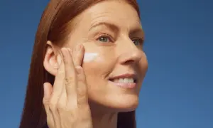 Donna con capelli rossi applica crema sul viso, contrastando la desquamazione della pelle.
