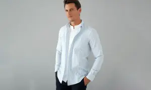 Uomo con camicia a righe azzurre e bianche, con colletto alla coreana e una camicia bianca sotto. La camicia con tasche è aperta, mostrando un look casual.