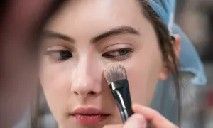 Una mano applica il fondotinta sul viso di una modella con un pennello. Ecco come applicare il fondotinta per un look impeccabile.