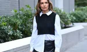 Donna con camicia asimmetrica bianca, gilet nero a coste e gonna in pelle nera.