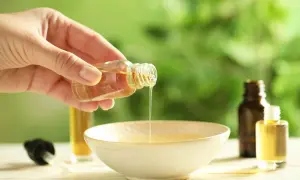 Mano versa un liquido dorato da una bottiglietta in una ciotola. È un olio per cuticole fatto in casa, perfetto per nutrire le unghie.