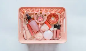 Cesto rosa pieno di trucchi: spray, lucidalabbra, fondotinta, ventilatore a forma di coniglietto, ciambella e altri accessori. Perfetti per viaggiare, i trucchi si possono portare in aereo!