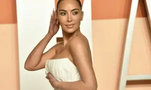 Kim Kardashian con un abito bianco senza spalline, posa con la mano tra i capelli.
