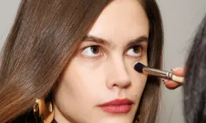 Come capire il colore del correttore online: un primo piano di una donna con pennello da trucco applicato sotto l'occhio.