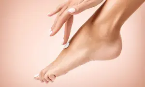 Mano con unghie bianche applica crema su un piede, un gesto di cura per un perfetto pedicure fai da te.