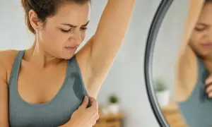 Donna con espressione di disagio controlla le ascelle bagnate, sintomo di sudore acido e stress.