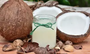 Un barattolo di olio di cocco, circondato da noci di cocco e gusci, pronto a rivelare i suoi benefici.