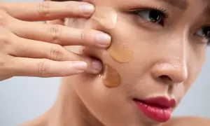 Dita sfumano campioni di fondotinta sul viso, mostrando a cosa serve il fondotinta per uniformare l'incarnato e coprire le imperfezioni.