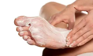 Mani che applicano una crema idratante su un piede, creando un impacco per piedi secchi fai da te per una pelle morbida e nutrita.