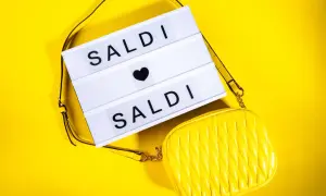 Scatola luminosa con "SALDI" e una borsa gialla. Scopri quanto durano i saldi estivi per fare acquisti convenienti!