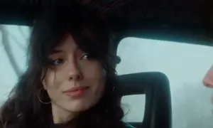 Ragazza con capelli scuri e orecchini a cerchio, guarda fuori dal finestrino, il cielo è celeste dalla porta.