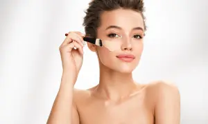 Donna applica fondotinta con pennello. Per un look naturale, il correttore deve essere più chiaro del fondotinta.