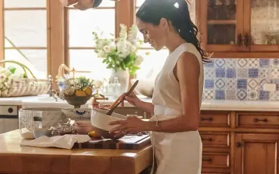 Meghan, Duchessa di Sussex, sorride mentre mescola in una ciotola in una cucina luminosa.