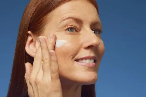 Donna con capelli rossi applica crema sul viso, contrastando la desquamazione della pelle.