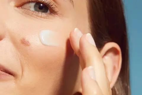 Dito, un dito applica una crema su una pelle ruvida con puntini bianchi, vicino all'occhio e alla bocca.