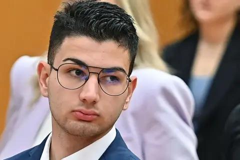 Alex Cotoia, con occhiali e abito blu, ascolta attentamente in tribunale.