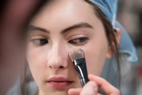 Una mano applica il fondotinta sul viso di una modella con un pennello. Ecco come applicare il fondotinta per un look impeccabile.