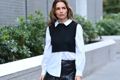 Donna con camicia asimmetrica bianca, gilet nero a coste e gonna in pelle nera.