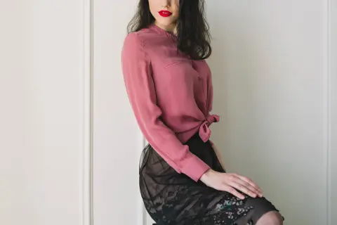 Donna con labbra rosse indossa una blusa in chiffon rosa annodata in vita e una gonna di pizzo nero.