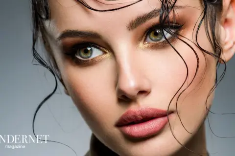 Occhi verdi intensi e labbra sensuali con un audace trucco grafico, capelli bagnati che incorniciano il viso.