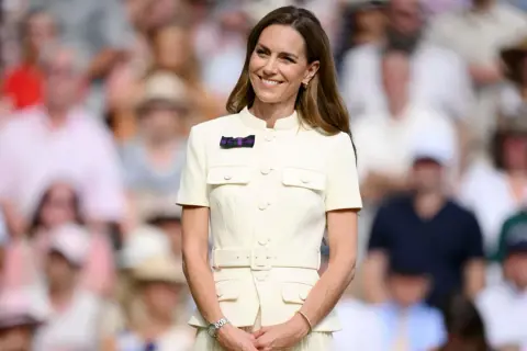 Kate Middleton sorride a Wimbledon, un'icona di stile in un abito chiaro, mentre il pubblico fa da sfondo sfocato.