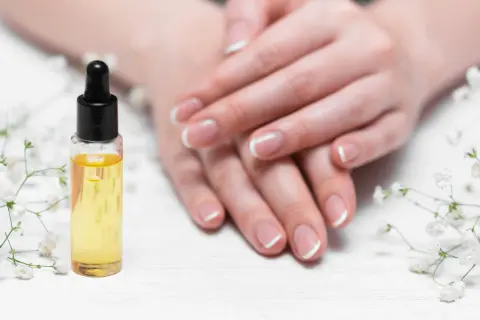 Olio per unghie e cuticole secche, con mani curate e fiori bianchi.