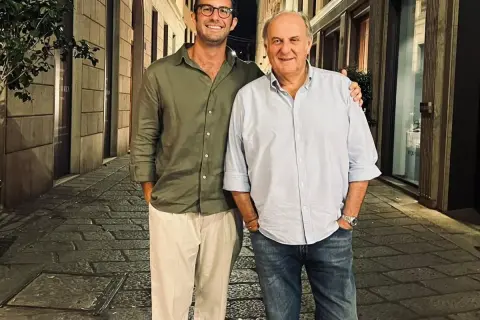 Edoardo Scotti sorride con un amico in una strada acciottolata di sera.