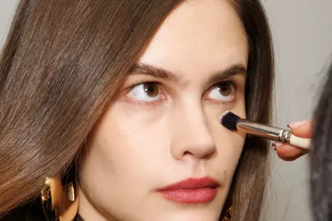Come capire il colore del correttore online: un primo piano di una donna con pennello da trucco applicato sotto l'occhio.