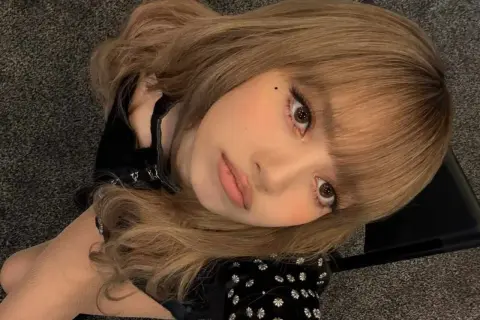 Primo piano di una giovane donna con capelli biondo cenere e carnagione media, che guarda verso l'alto con un'espressione dolce.