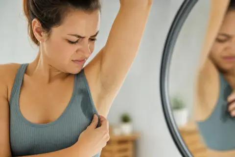 Donna con espressione di disagio controlla le ascelle bagnate, sintomo di sudore acido e stress.