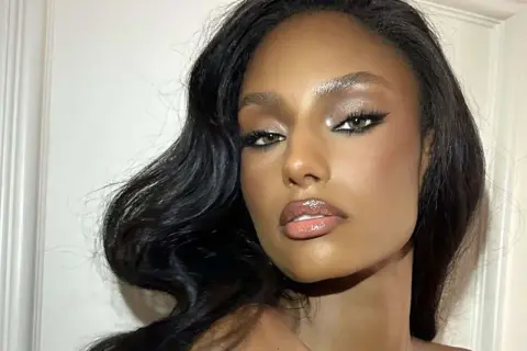 Volto di donna con trucco da sera elegante: occhi definiti da eyeliner e ombretto luminoso, labbra glossate. Capelli scuri e ondulati.