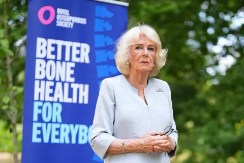 Camilla, regina consorte del Regno Unito, sorride con un banner della Royal Osteoporosis Society alle spalle.