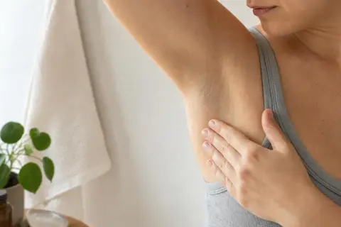 Mano che sfiora l'ascella, un gesto che ci ricorda perchè il sudore puzza e come prendersene cura.