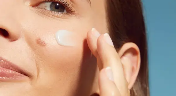 Dito, un dito applica una crema su una pelle ruvida con puntini bianchi, vicino all'occhio e alla bocca.