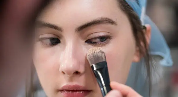 Una mano applica il fondotinta sul viso di una modella con un pennello. Ecco come applicare il fondotinta per un look impeccabile.