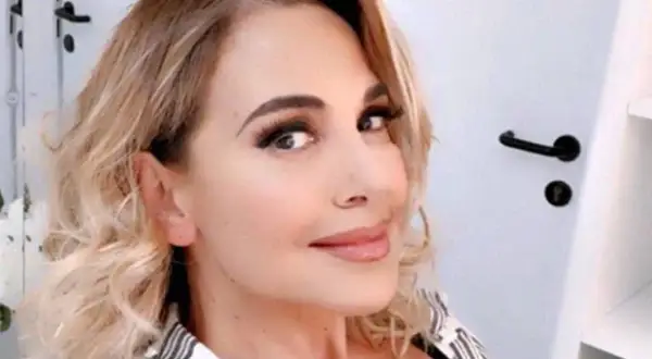Barbara D'Urso sorride con capelli biondi mossi e trucco accentuato.