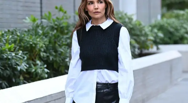 Donna con camicia asimmetrica bianca, gilet nero a coste e gonna in pelle nera.