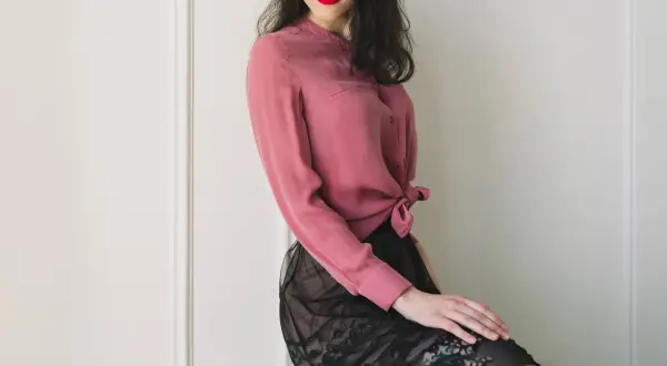 Donna con labbra rosse indossa una blusa in chiffon rosa annodata in vita e una gonna di pizzo nero.