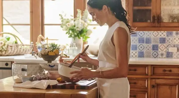 Meghan, Duchessa di Sussex, sorride mentre mescola in una ciotola in una cucina luminosa.