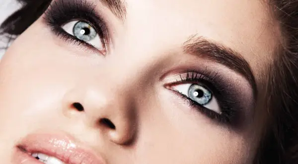 Occhi azzurri con un intenso trucco smokey eyes, labbra lucide e pelle luminosa.