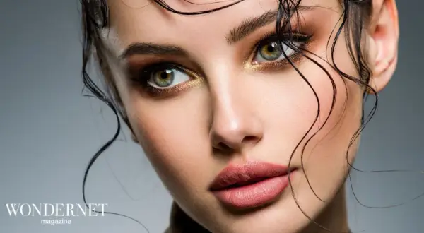 Occhi verdi intensi e labbra sensuali con un audace trucco grafico, capelli bagnati che incorniciano il viso.