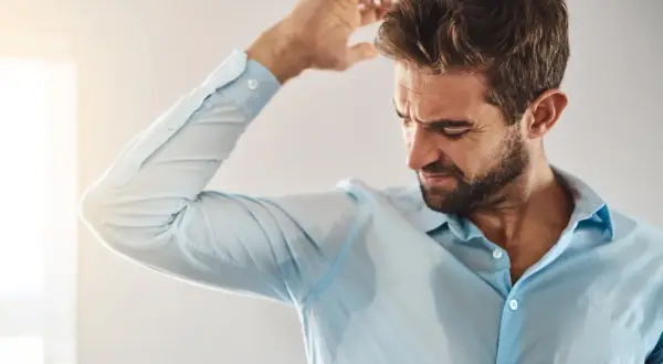 Uomo con camicia bagnata di sudore, preoccupato per le cause del sudore acido.