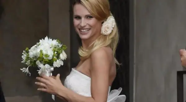 Michelle Hunziker sorride con un bouquet, indossando un abito da sposa che ricorda quello del suo matrimonio con Eros Ramazzotti.