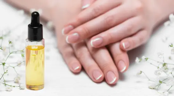 Olio per unghie e cuticole secche, con mani curate e fiori bianchi.