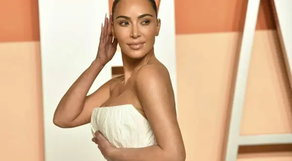 Kim Kardashian con un abito bianco senza spalline, posa con la mano tra i capelli.