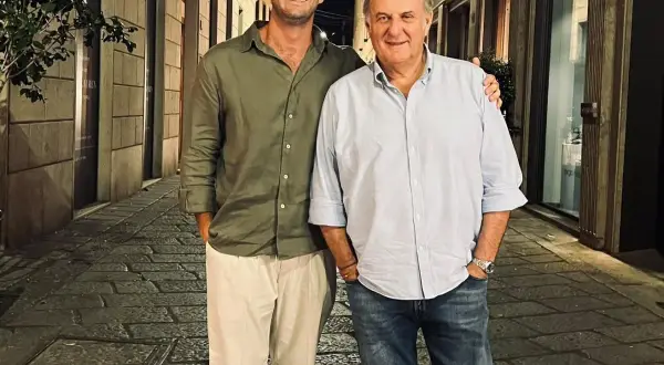 Edoardo Scotti sorride con un amico in una strada acciottolata di sera.