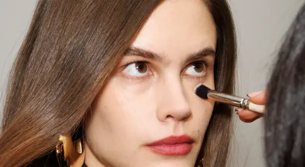 Come capire il colore del correttore online: un primo piano di una donna con pennello da trucco applicato sotto l'occhio.