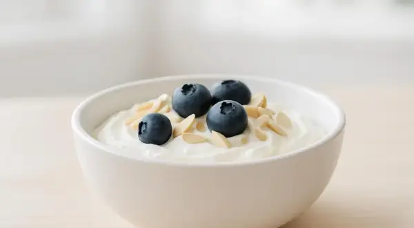 Una ciotola di yogurt bianco con mirtilli e mandorle a lamelle, perfetta per uno spuntino serale leggero e nutriente.