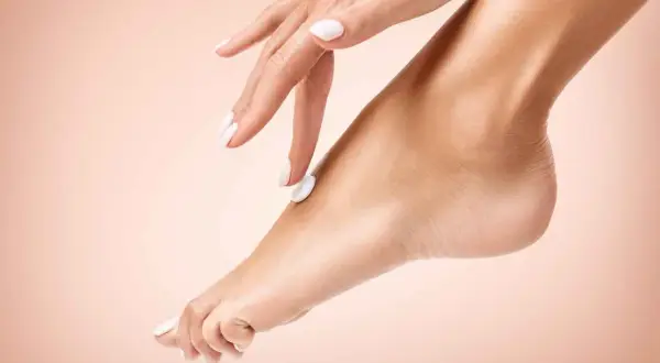 Mano con unghie bianche applica crema su un piede, un gesto di cura per un perfetto pedicure fai da te.