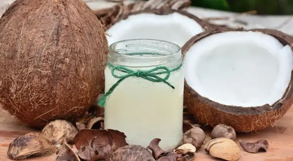 Un barattolo di olio di cocco, circondato da noci di cocco e gusci, pronto a rivelare i suoi benefici.